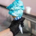Blue ice cream cone in gloved hand.