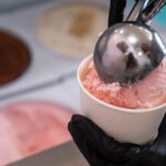 Scooping strawberry ice cream into a cup.